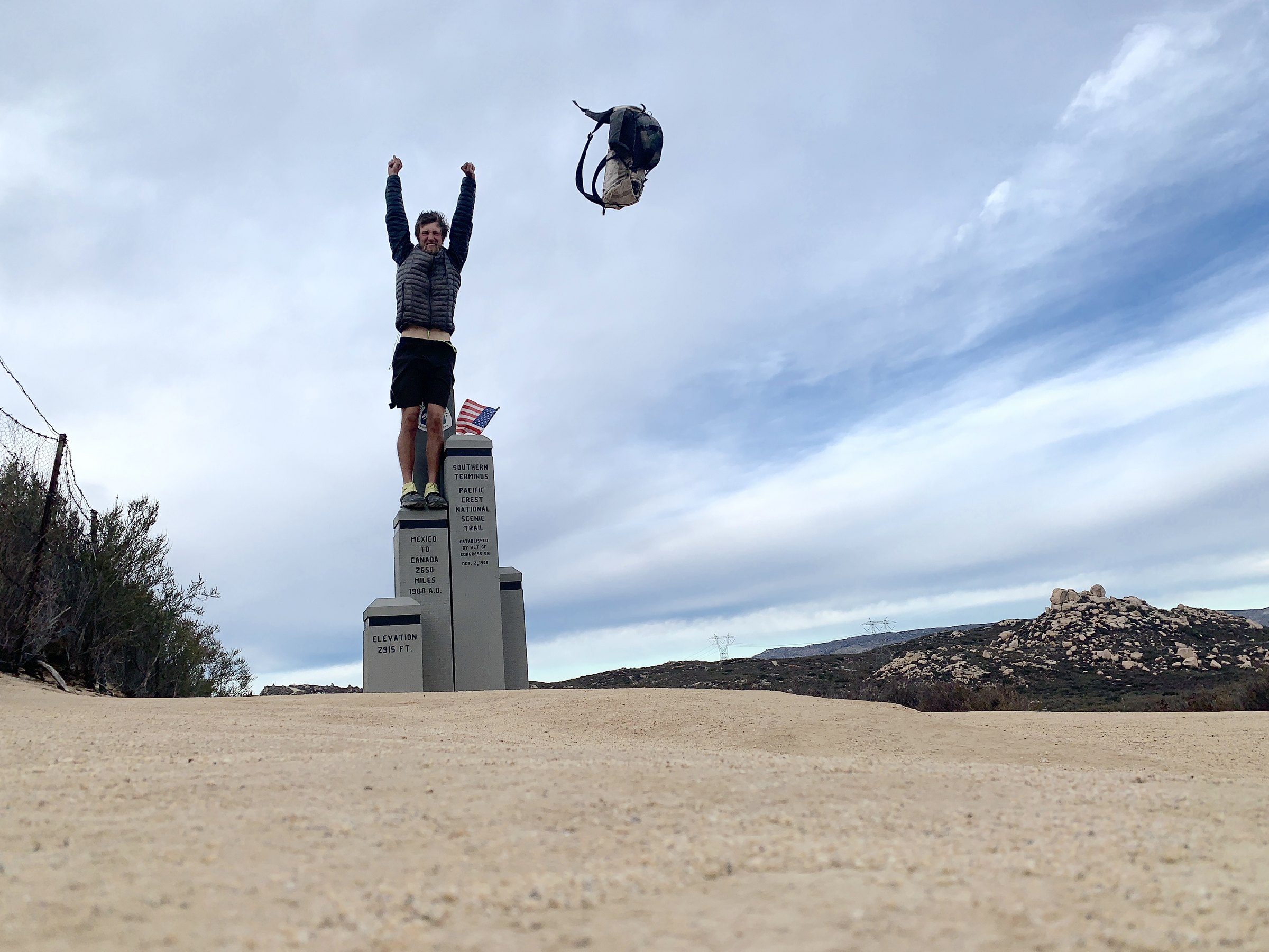 Two hikers jumping beside a border monument